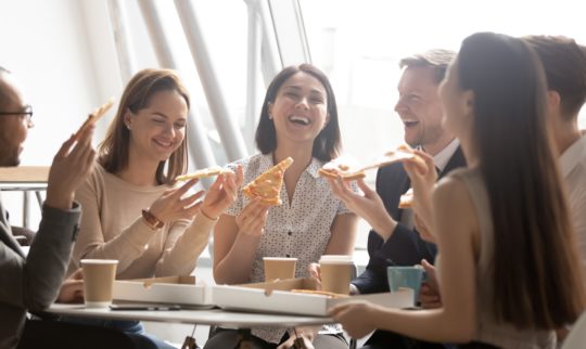 En gjeng kollegaer sitter sammen og spiser pizza.